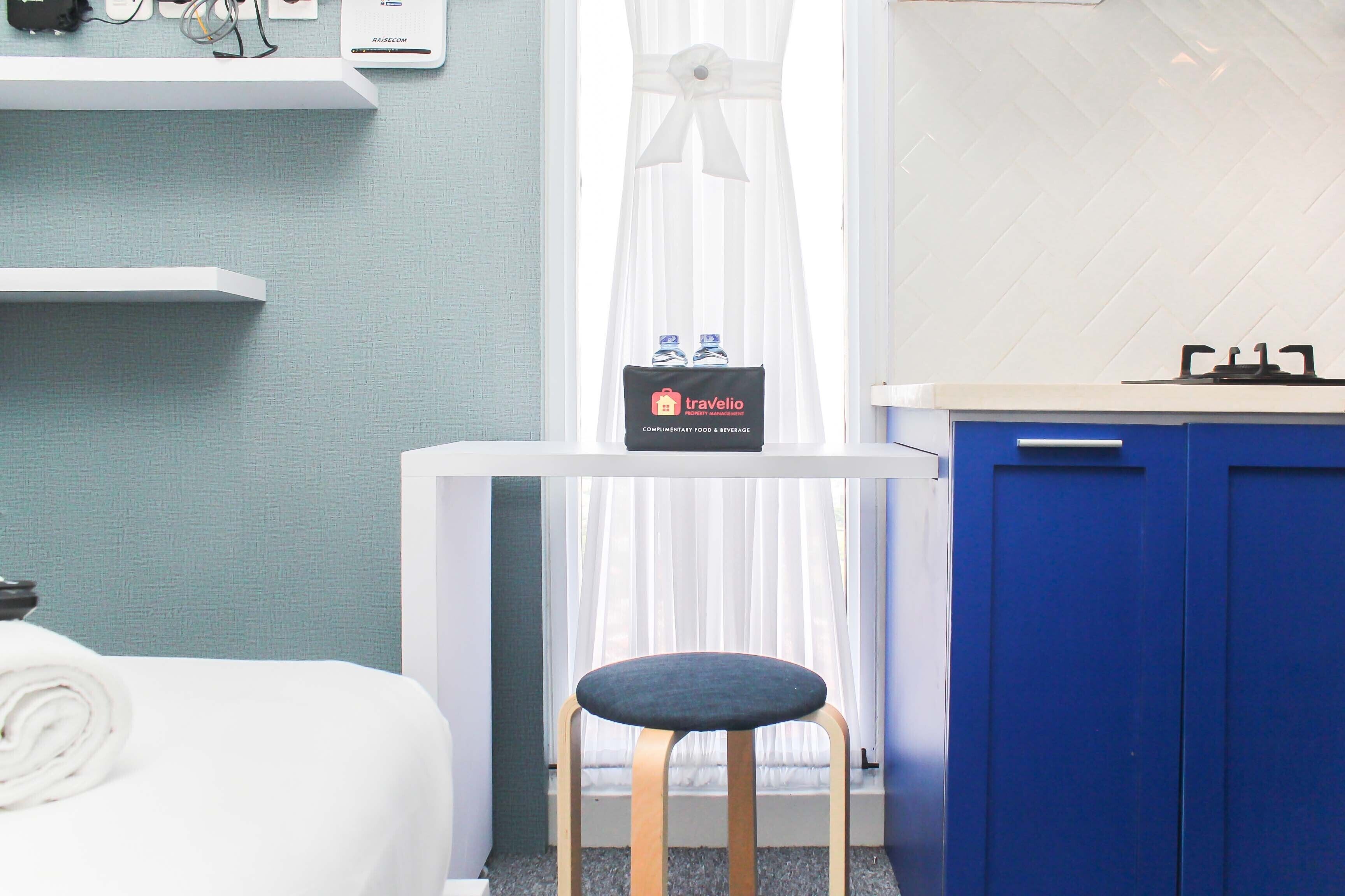 Una habitación de hotel con cama, una mesita de noche con artículos de aseo, un armario azul y una ventana con cortinas translúcidas.