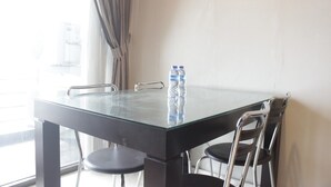 A glass-top table with two chairs, a bottle of water, and a window with curtains. - Deluxe 2Br At Dago Boutique Apartment (Bandung)