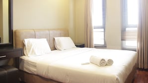 A hotel room with a large bed, two pillows, a bedside table, a mirror, and a window with curtains. - Deluxe 2Br At Dago Boutique Apartment (Bandung)