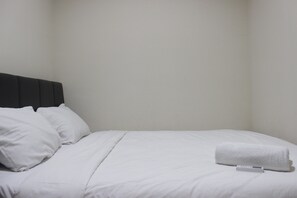 A neatly made bed with white linens and pillows, a black headboard, and a folded white towel on the bed. - Deluxe 2Br At Dago Boutique Apartment (Bandung)