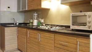 A kitchen with wooden cabinets, a stove, a microwave, and a blender. - Deluxe 2Br At Dago Boutique Apartment (Bandung)