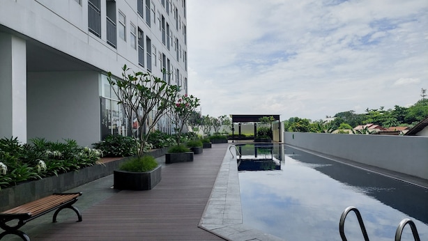 A modern outdoor pool area with a wooden deck, benches, and a clear sky. - Comfort Living Studio Room At Serpong Garden Apartment (Cisauk)
