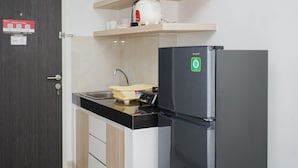 A compact kitchen with a black refrigerator, a sink, and wooden cabinets. - Comfort Living Studio Room At Serpong Garden Apartment (Cisauk)