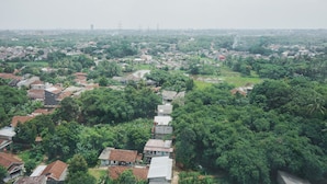 An aerial view of a densely populated residential area with numerous houses, surrounded by lush greenery. - Comfort Living Studio Room At Serpong Garden Apartment (Cisauk)