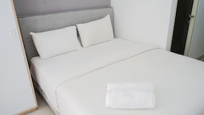 A neatly made bed with white bedding and pillows, a grey headboard, and a white towel on the bed. - Comfort Living Studio Room At Serpong Garden Apartment (Cisauk)