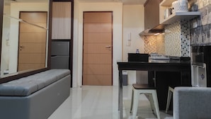 A compact kitchen with a built-in refrigerator, a dining table with a stool, and a bench. - Chic And Cozy 2Br At Vida View Apartment (Makassar)