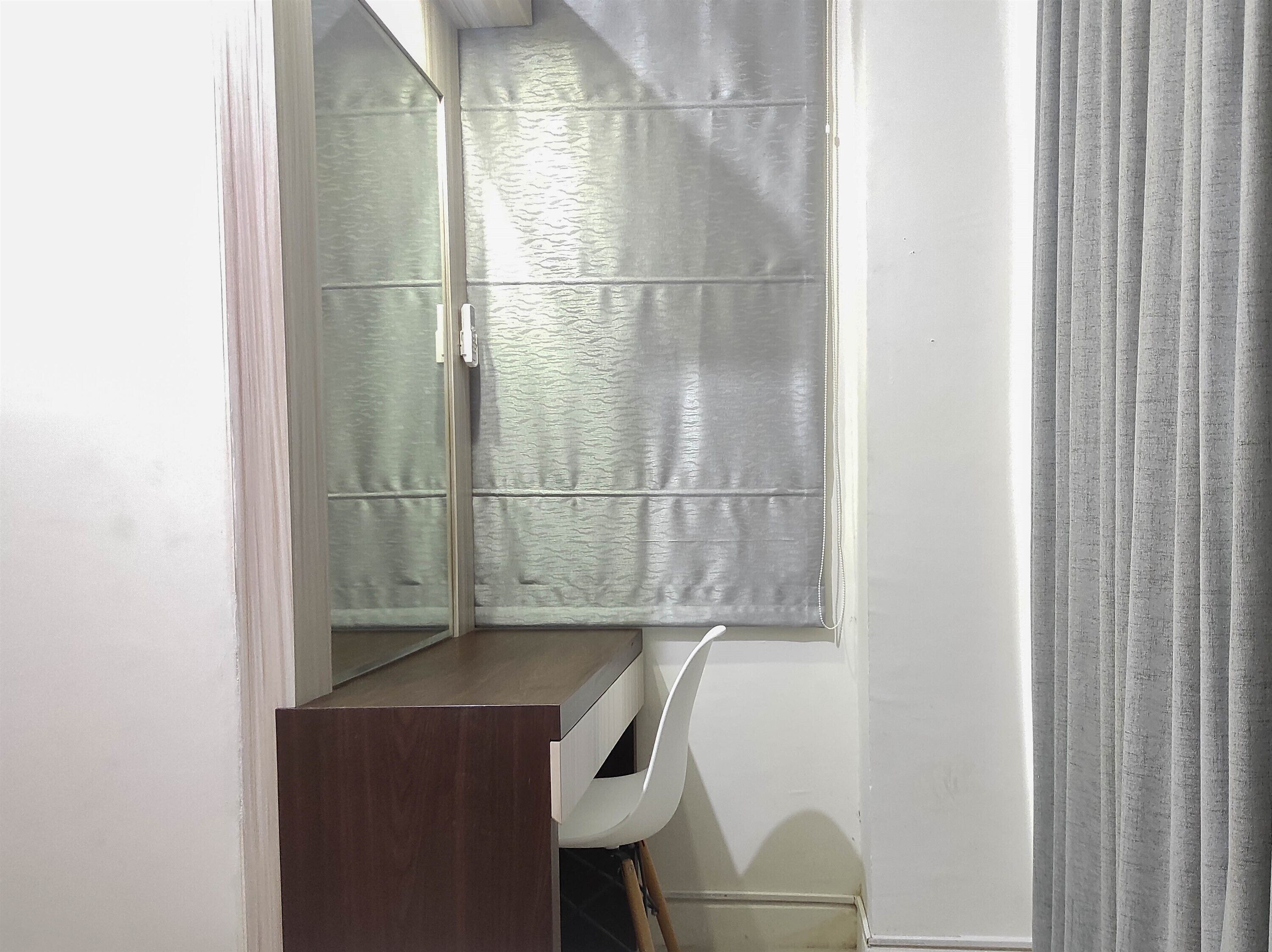 A small, enclosed bathroom with a mirror, a wooden cabinet, and a window with frosted glass.