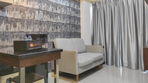 A modern living room with a sofa, a coffee table, and a wall with a cityscape wallpaper. There is a tray table with a tray and two bottles. - Chic And Cozy 2Br At Vida View Apartment (Makassar)