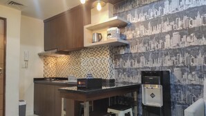 A modern kitchen with a cityscape wallpaper, a stainless steel refrigerator, and a coffee maker on the counter. - Chic And Cozy 2Br At Vida View Apartment (Makassar)