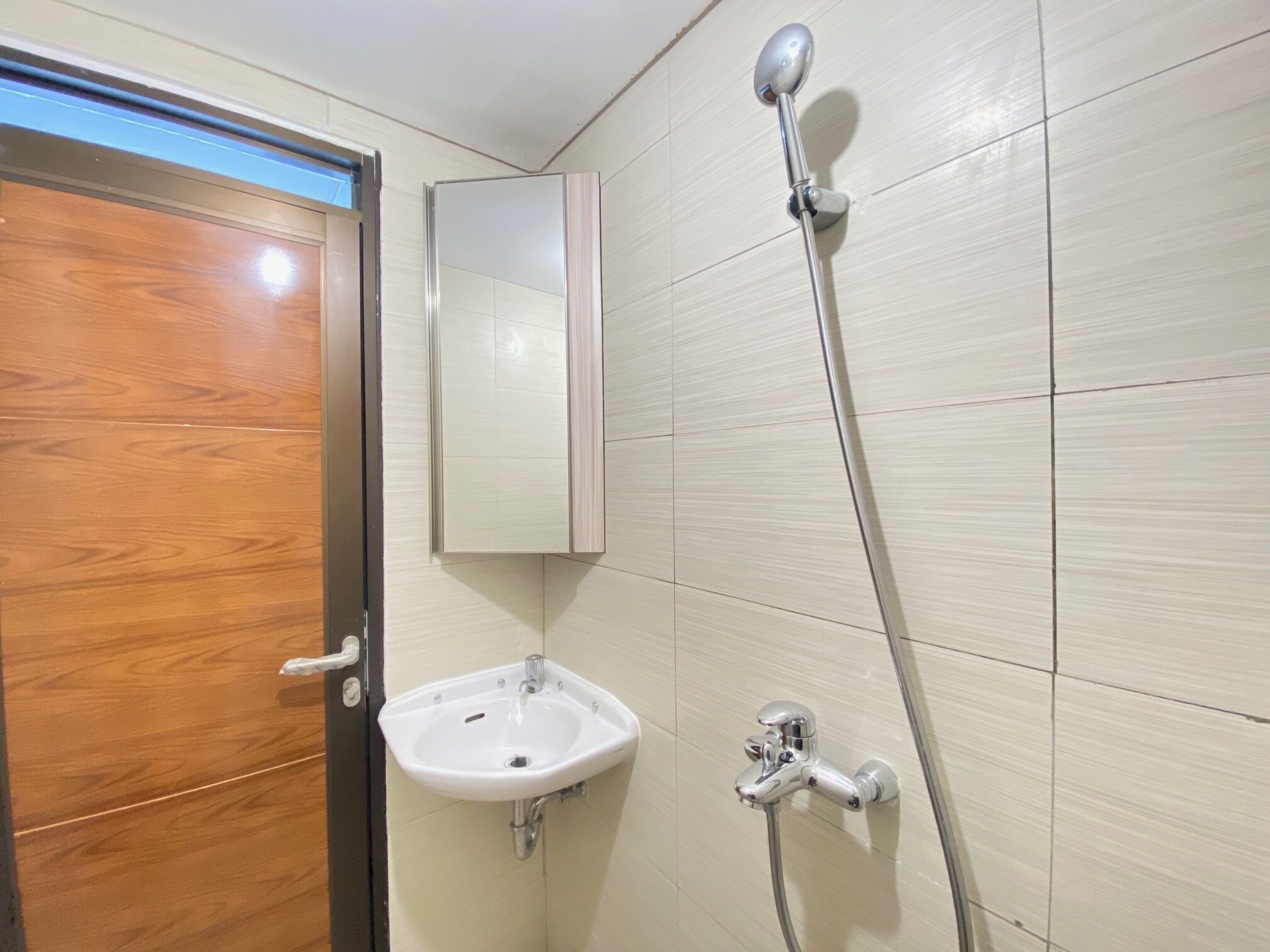 A bathroom with a wooden door, a white sink, a mirror, and a shower.