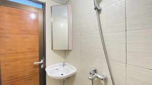 A bathroom with a wooden door, a white sink, a mirror, and a shower. - Modern And Cozy Studio Room At Gateway Pasteur Apartment (Cimahi)