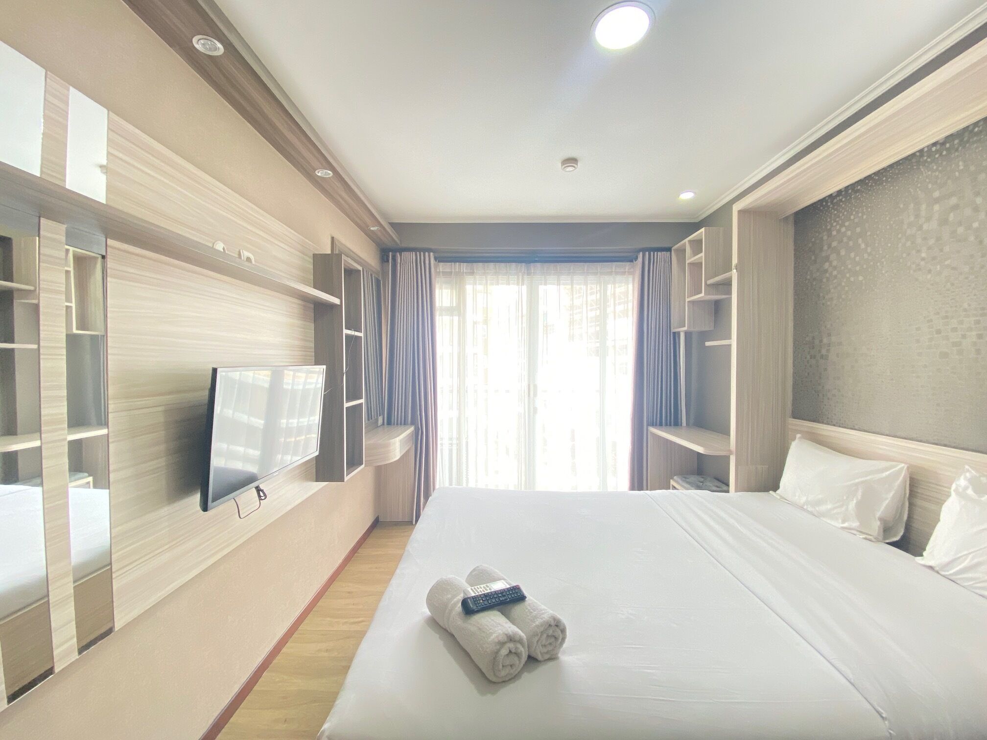 Habitación de hotel con una cama grande, un televisor de pantalla plana montado en la pared y estanterías empotradas.