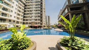 A modern residential building with a central swimming pool surrounded by lush greenery. - Modern And Cozy Studio Room At Gateway Pasteur Apartment (Cimahi)