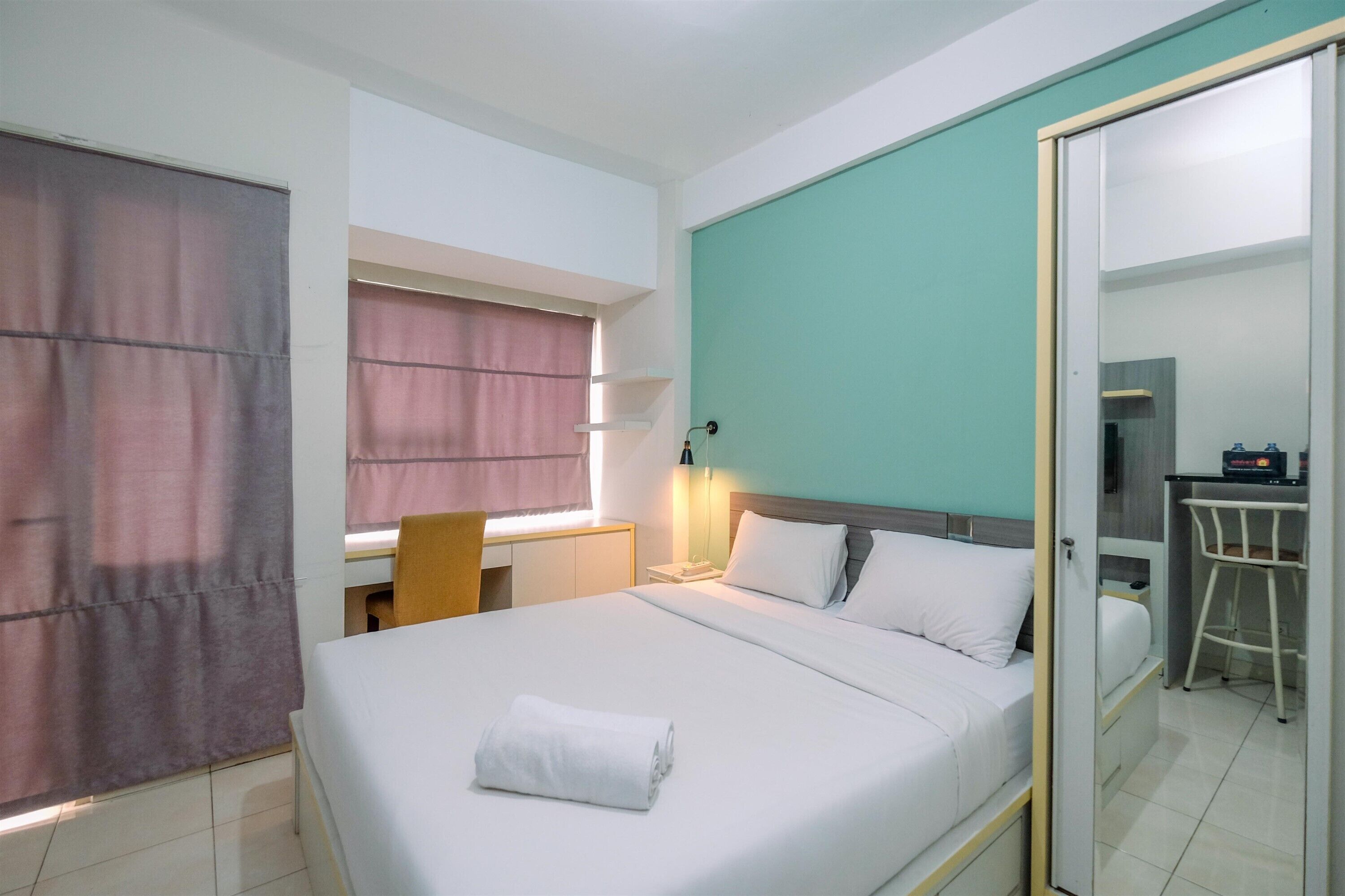Habitación de hotel con cama, escritorio, silla, espejo y una pequeña kitchenette.