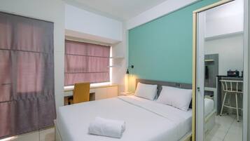 Habitación de hotel con cama, escritorio, silla, espejo y una pequeña kitchenette.