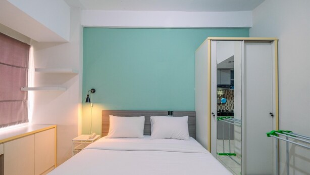 A hotel room with a bed, a nightstand, a lamp, a wardrobe, and a bathroom visible through a mirror. - Warm And Cozy Studio Apartment Margonda Residence 5 Near Campus (Depok)