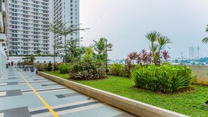 A modern urban walkway with a tiled path, green landscaping, and tall residential buildings in the background. - Warm And Cozy Studio Apartment Margonda Residence 5 Near Campus (Depok)