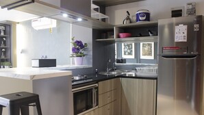 A modern kitchen with a stainless steel refrigerator, a microwave, and a sink. There is a bar stool and a potted plant on the counter. - Modern & Cozy 2Br Apartment At Tamansari Tera Residence (Bandung)