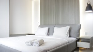 A modern bedroom with a large bed, a nightstand, and a wall-mounted lamp. - Modern & Cozy 2Br Apartment At Tamansari Tera Residence (Bandung)