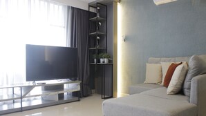 A modern living room with a flat-screen TV, a glass coffee table, a grey sofa, and a black shelving unit with plants. - Modern & Cozy 2Br Apartment At Tamansari Tera Residence (Bandung)
