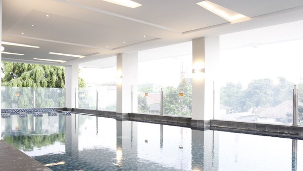 An indoor swimming pool with clear glass walls, tiled floor, and ceiling lights. - Modern & Cozy 2Br Apartment At Tamansari Tera Residence (Bandung)