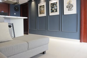 A modern living room with a grey sofa, a clock on the wall, and framed artwork.