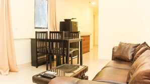 Una sala de estar con un sofá de cuero marrón, una mesa de centro de vidrio, un mueble de TV negro y un comedor con una mesa y sillas negras.