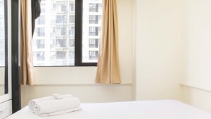 Habitación de hotel con cama, ventana con cortinas y vista a un edificio.