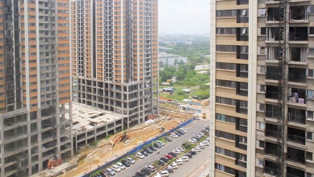 Un edificio de gran altura en construcción, con varios pisos, un estacionamiento al frente y una obra cercana.