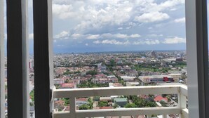 A cityscape viewed from a balcony with a railing, featuring a mix of residential and commercial buildings under a partly cloudy sky.