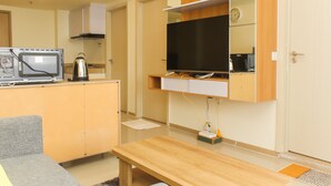 Un espacio habitable compacto con kitchenette, un televisor de pantalla plana montado en una pared de madera, un sofá gris y una mesa de madera.