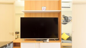 Una sala moderna con un televisor de pantalla plana montado en un mueble de madera, un estante con adornos y un sofá con un cojín amarillo.