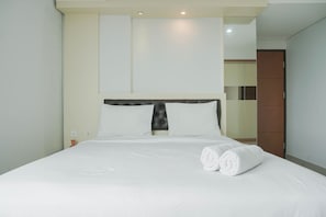 A neatly made bed with white linens and two rolled towels, a modern headboard, and a large mirror on the wall.