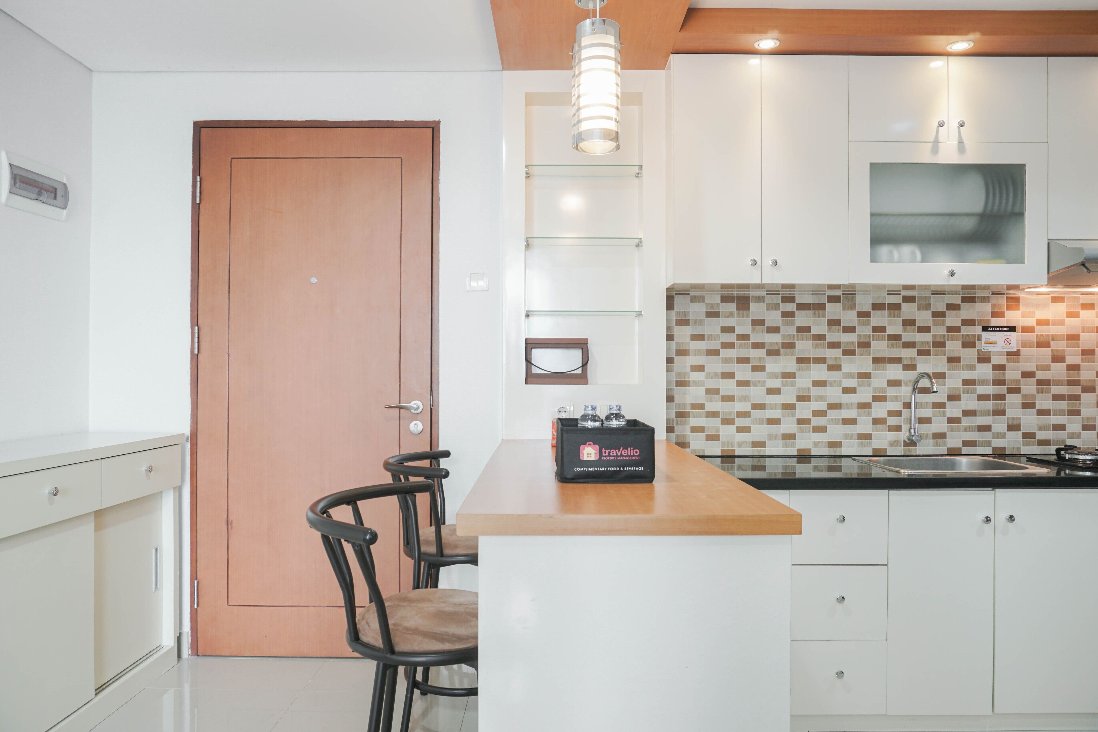 Une cuisine moderne avec des meubles blancs, une porte en bois, une étagère en verre et une boîte de la marque Travello.