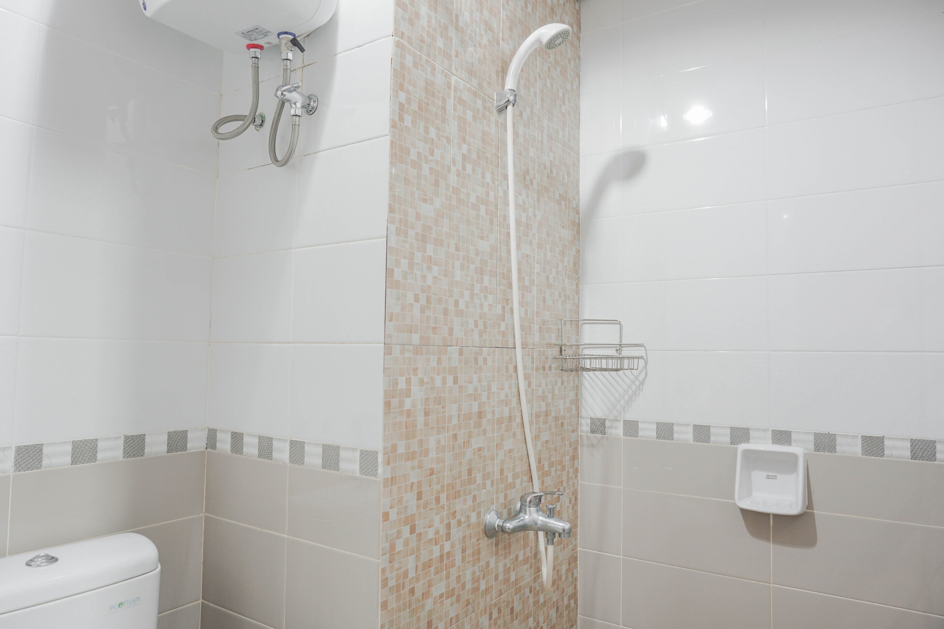 A bathroom with a shower, toilet, and a soap dispenser on the wall.