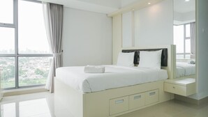 A modern bedroom with a large bed, a nightstand, a mirror, and a view of the city through a large window. - Warm And Cozy 3Br Apartment At The Royal Olive Residence (Jakarta)