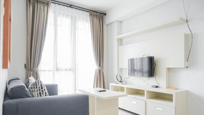 A modern living room with a sofa, TV, and a white entertainment unit. - Warm And Cozy 3Br Apartment At The Royal Olive Residence (Jakarta)