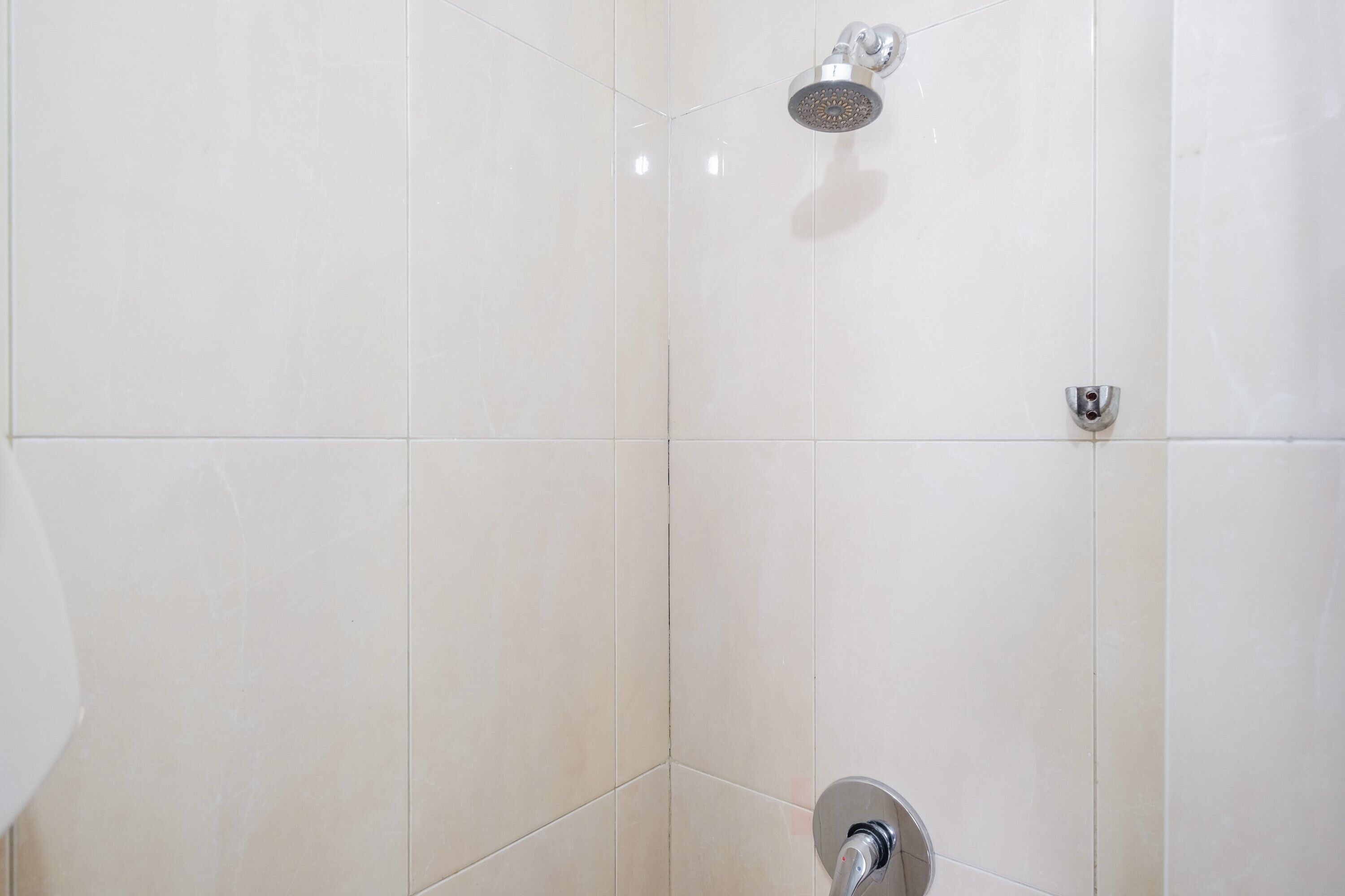 A bathroom with white tiles, a showerhead, and a faucet.