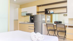 A hotel room with a bed, a desk, a chair, a refrigerator, a microwave, and a coffee maker.