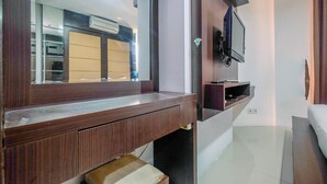 A modern hotel room with a wooden vanity, a large mirror, a flat-screen TV mounted on the wall, and a neatly made bed. - Best Deal Studio Apartment At Mangga Dua Residence (Jakarta)