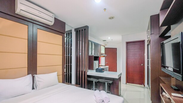 A hotel room with a bed, a desk, a television, and an air conditioning unit. - Best Deal Studio Apartment At Mangga Dua Residence (Jakarta)