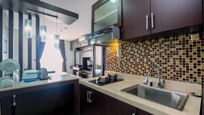 A modern kitchen with dark wooden cabinets, a tiled backsplash, and stainless steel appliances. - Comfort And Homey Studio Apartment At Mangga Dua Residence (Jakarta)