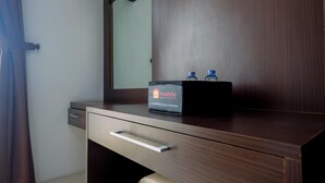 A wooden dresser with a mirror, a drawer, and a box labeled "Travelio" containing bottled water. - Comfort And Homey Studio Apartment At Mangga Dua Residence (Jakarta)