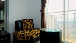 A modern living room with a sofa and a glass-top table, large windows with curtains, and a view of a cityscape. - Comfort And Homey Studio Apartment At Mangga Dua Residence (Jakarta)