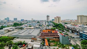 A cityscape with various buildings, including a prominent multi-story structure with a red roof and a large warehouse-like building. - Cozy Living Studio Apartment Mangga Dua Residence Near Itc Mall (Jakarta)