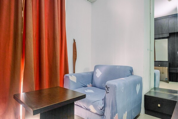 Une pièce avec un canapé bleu, une table en bois, un miroir et un rideau rouge.