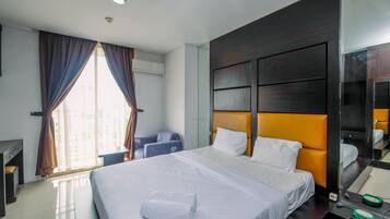 A hotel room with a large bed, a desk, a chair, and a window with curtains.