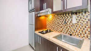 A kitchen with dark wooden cabinets, a stainless steel sink, a tiled backsplash, and a gas stove. - Cozy Living Studio Apartment Mangga Dua Residence Near Itc Mall (Jakarta)