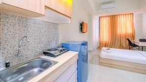 A compact hotel room with a kitchenette, a bed, a desk, and a window with curtains.
