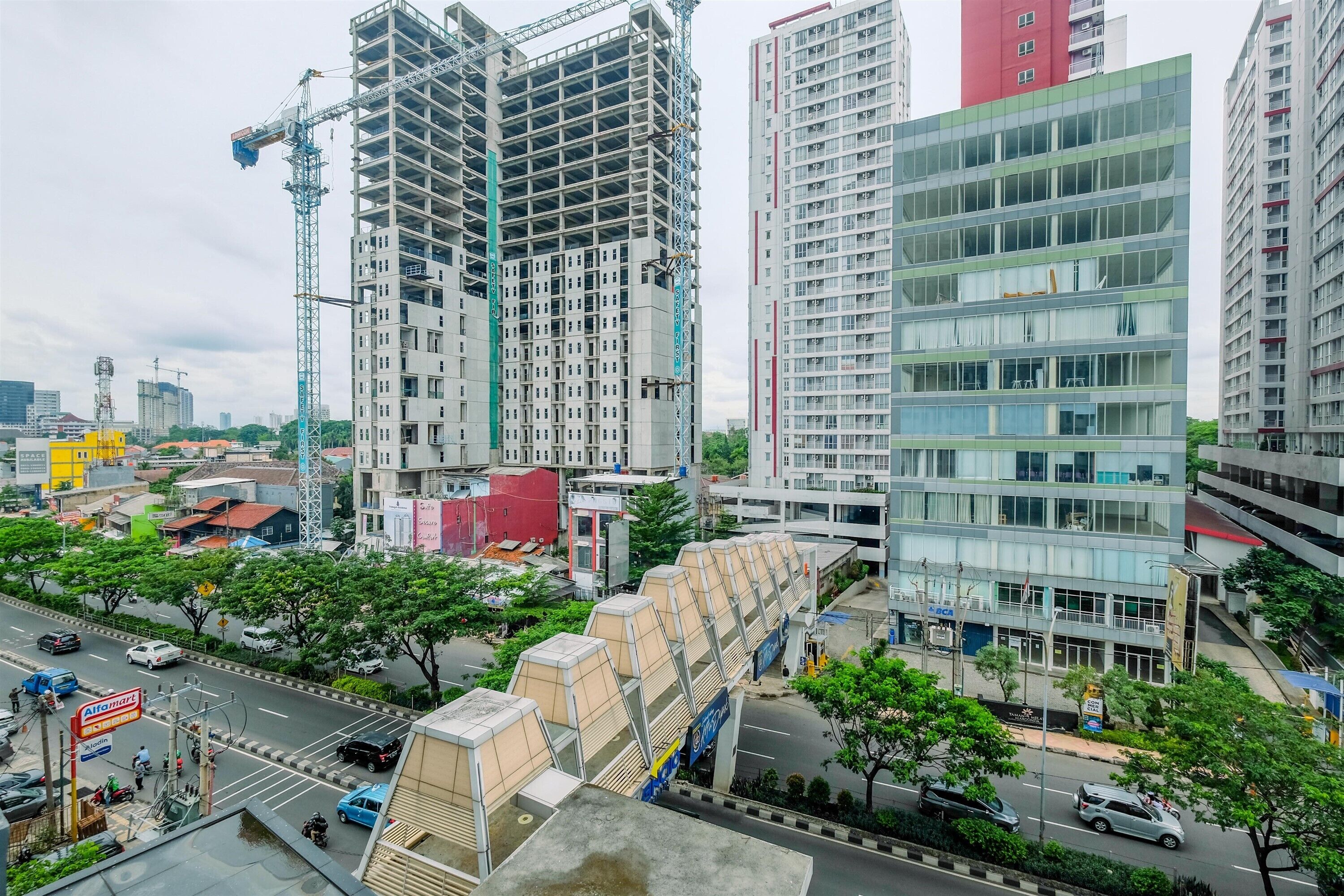 A high-rise building under construction with a crane, surrounded by other buildings and a busy street with vehicles and pedestrians.
